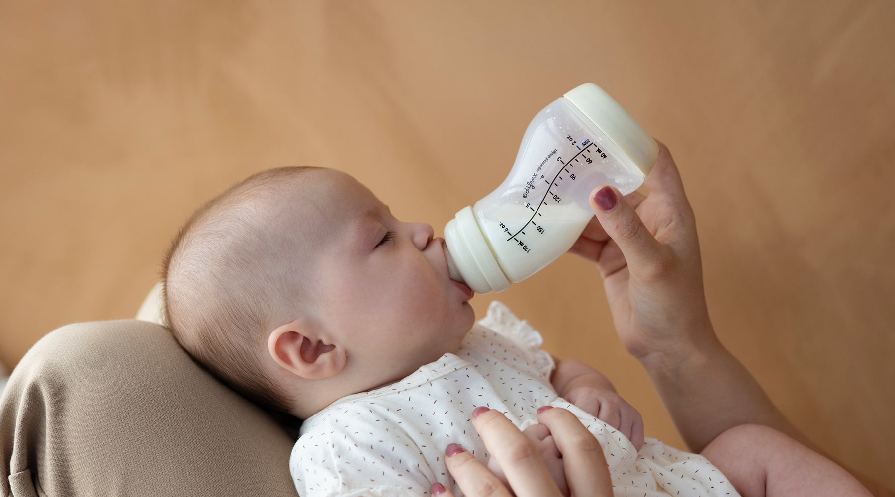 Baby drinkt uit een fles met volumeaanduidingen terwijl een volwassene de fles vasthoudt