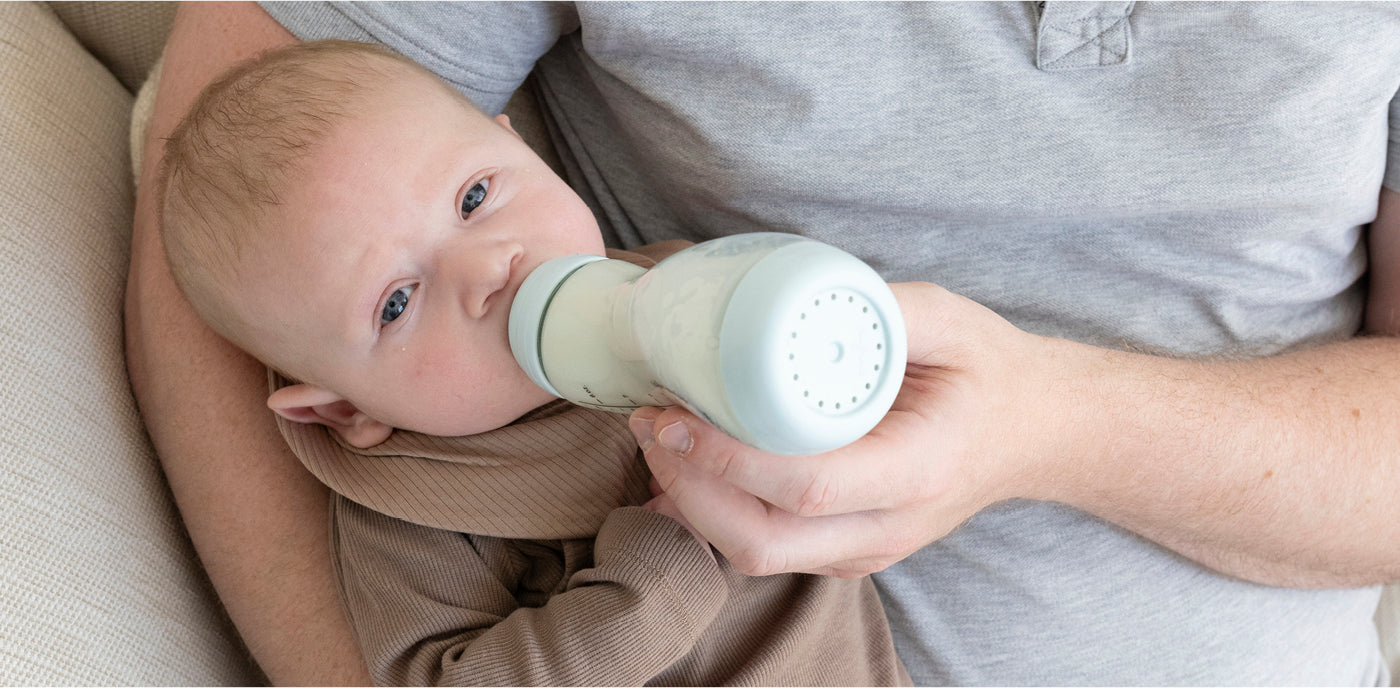 aby drinkt ontspannen uit mintgroene Difrax anti-colic fles in armen van ouder in grijs shirt
