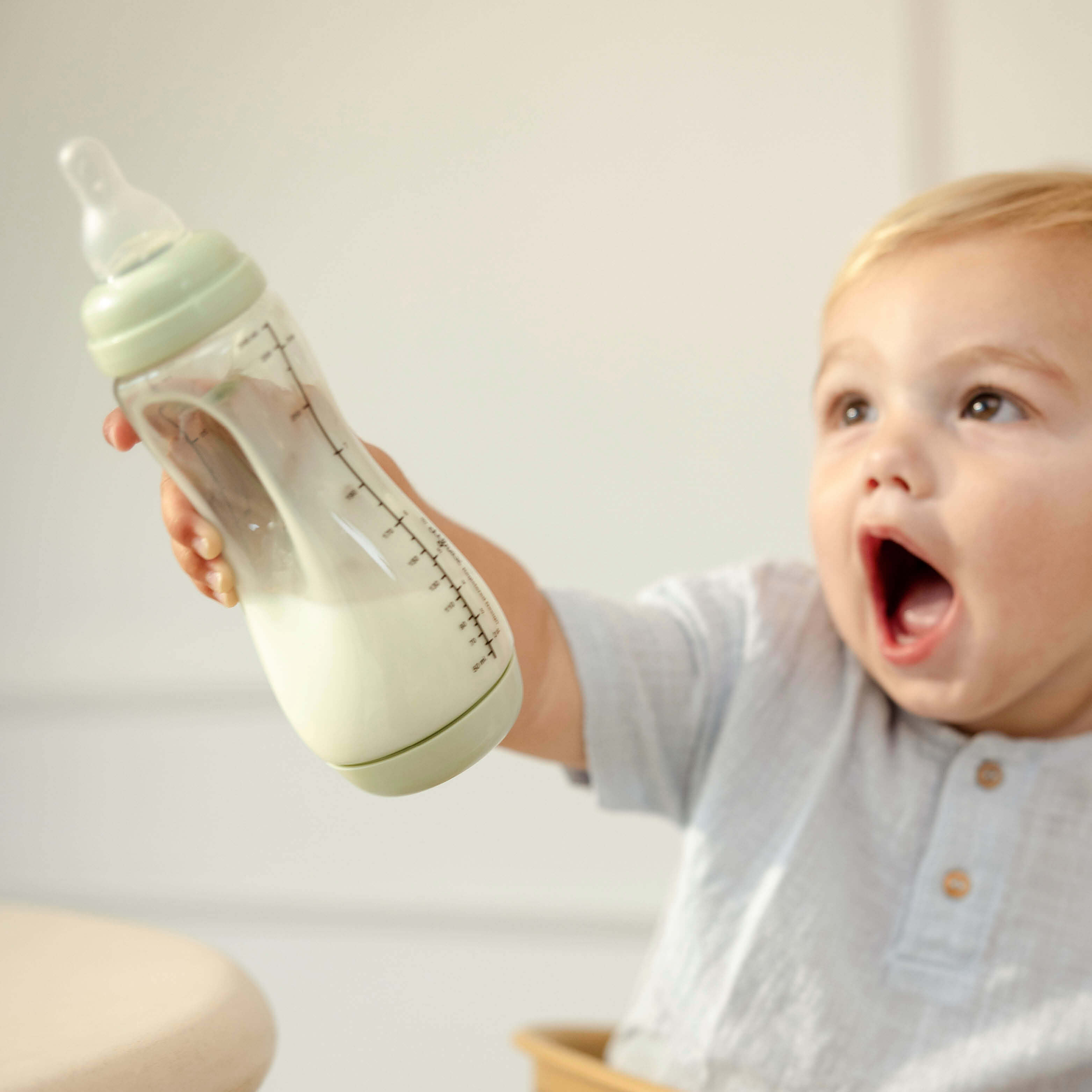 Baby houdt enthousiast Difrax Easy Grip pistachgroene fles omhoog, zelfstandig drinken met natuurlijke speen