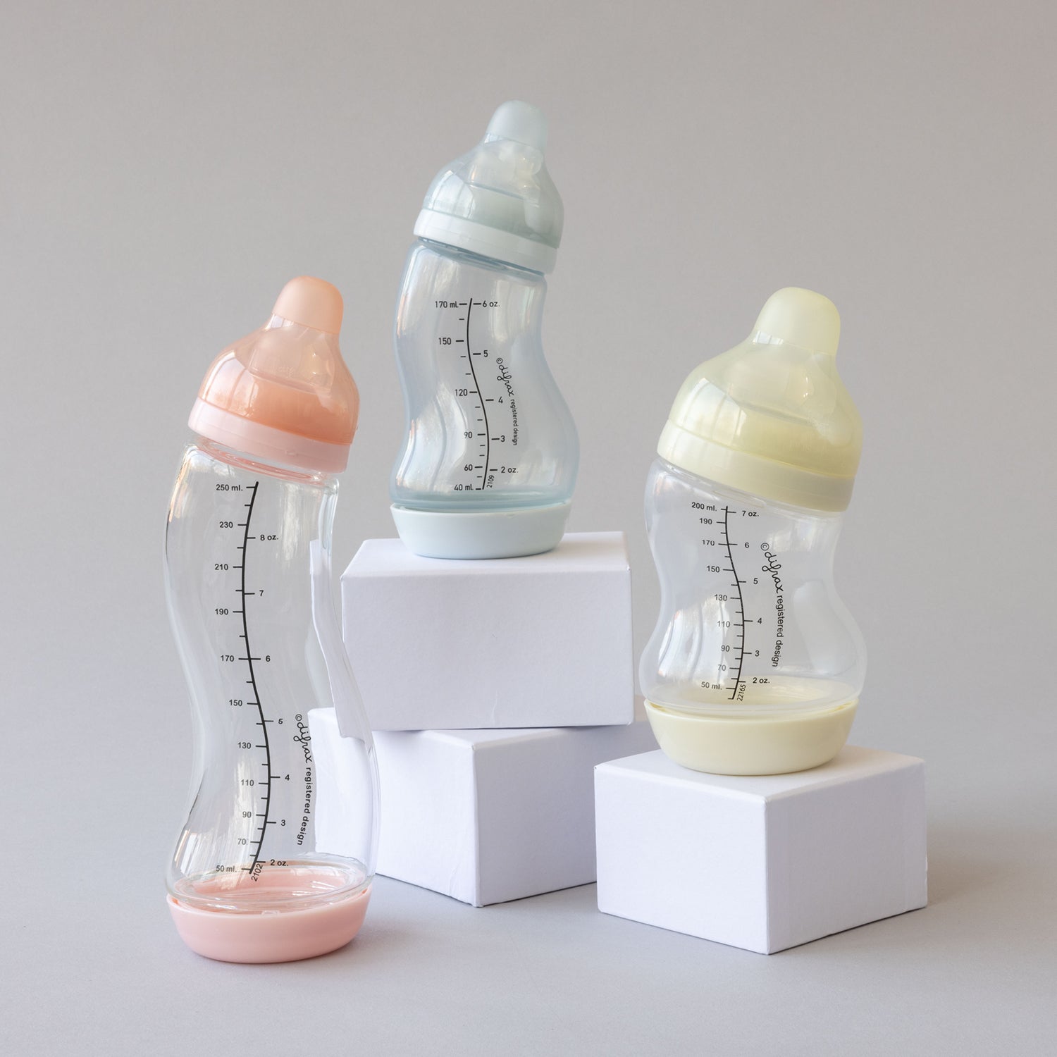 glazen babyflessen op blokjes in roze, blauw en crème kleur