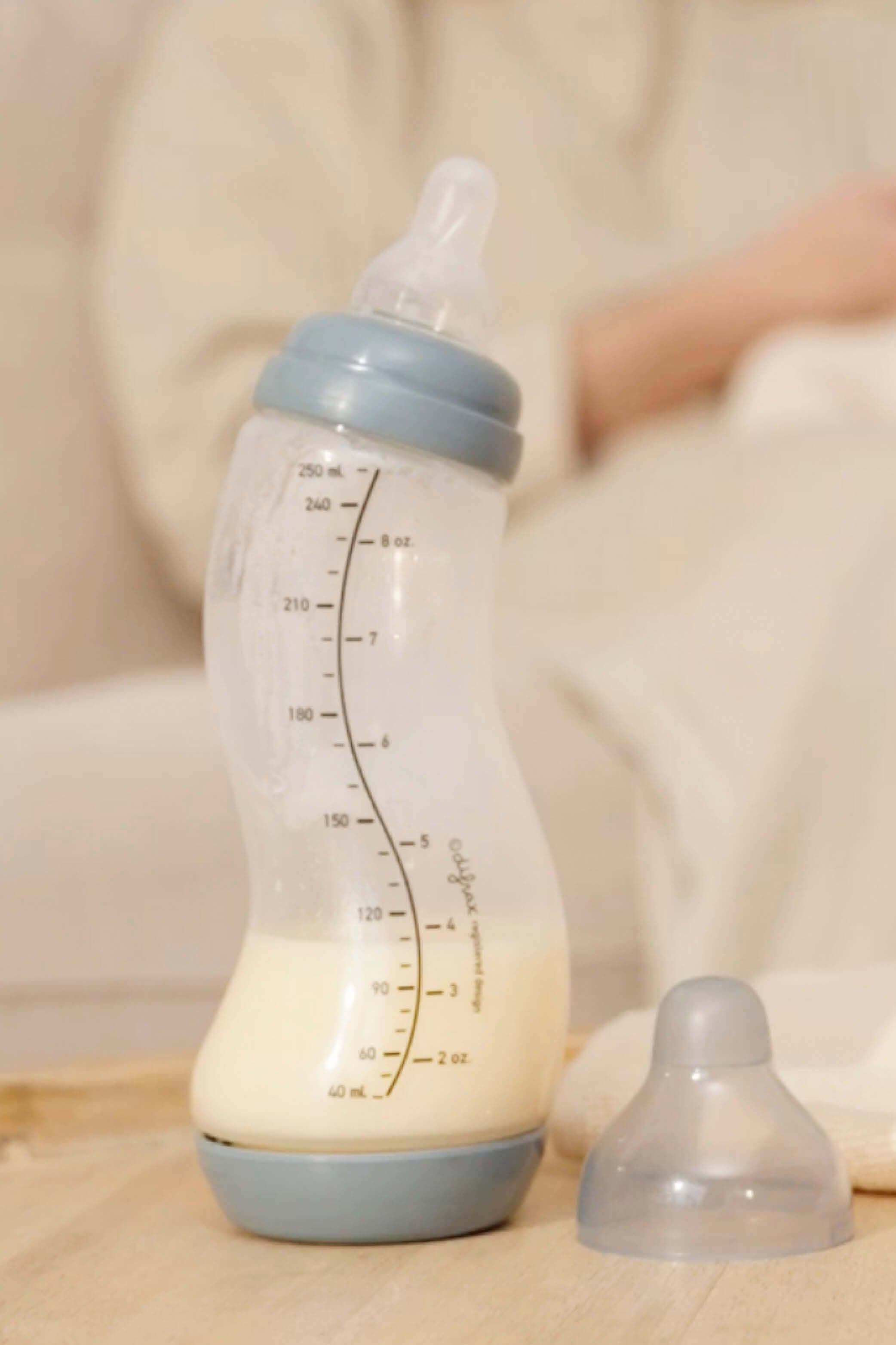 Stone grijze Difrax S-fles 250ml gevuld met moedermelk op houten ondergrond, slapende baby op zachte deken op achtergrond