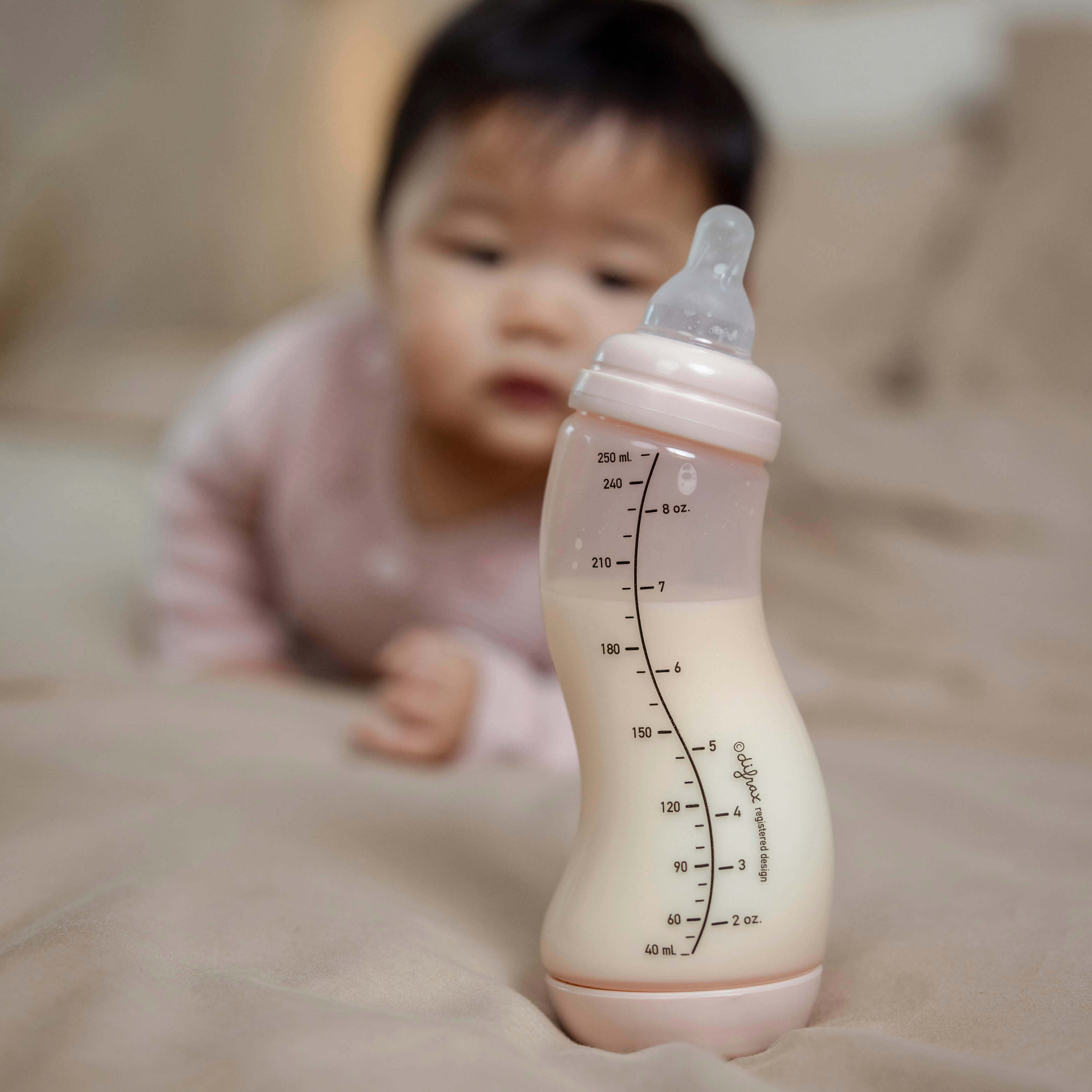 Close-up van roze Difrax S-fles 250ml gevuld met moedermelk, baby op de achtergrond, focus op volumemaatverdeling tot 250ml