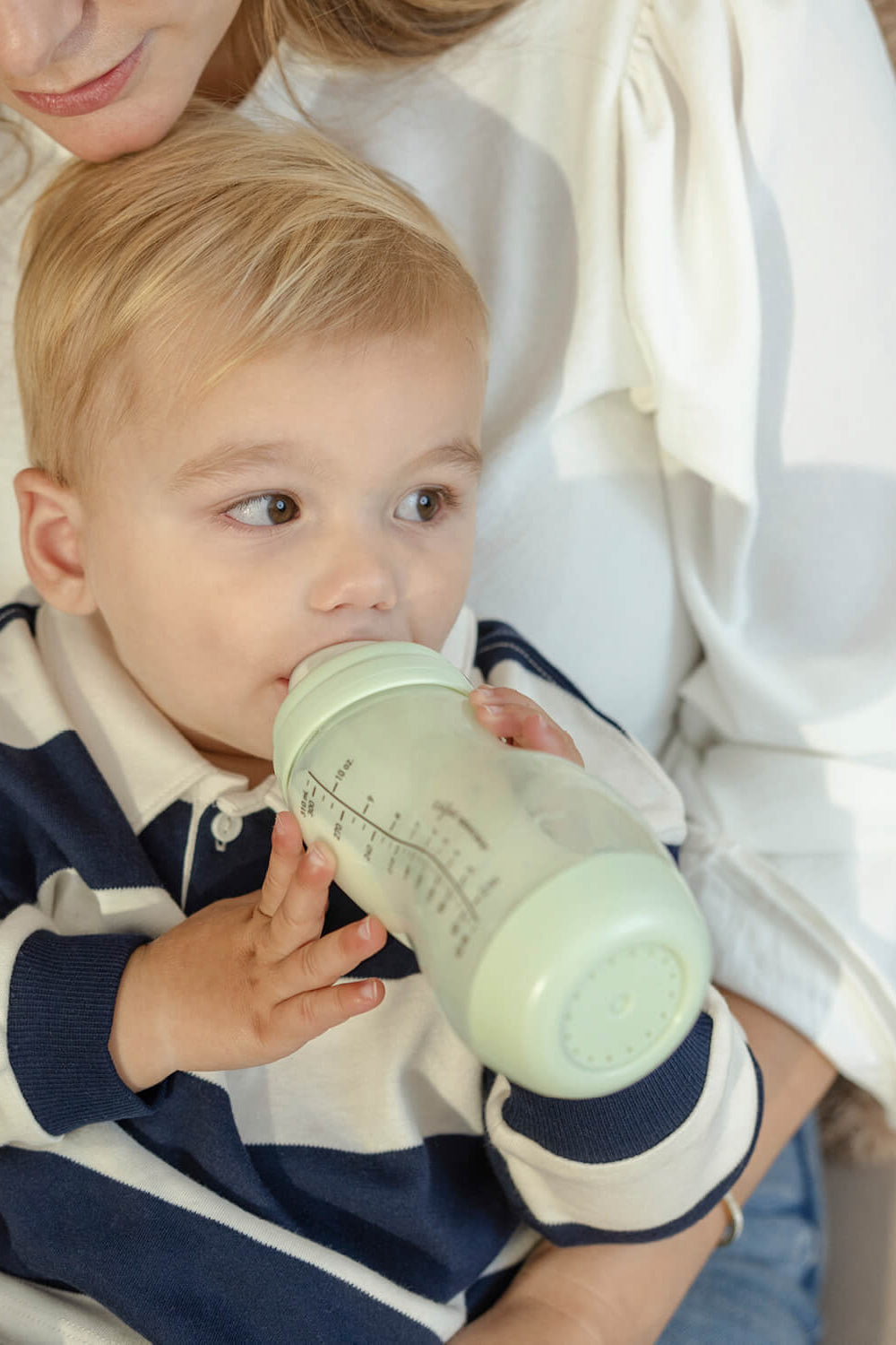 Peuter drinkt zelfstandig uit pistachgroene Difrax S-fles 310ml bij moeder, stimulering van zelfstandig drinken