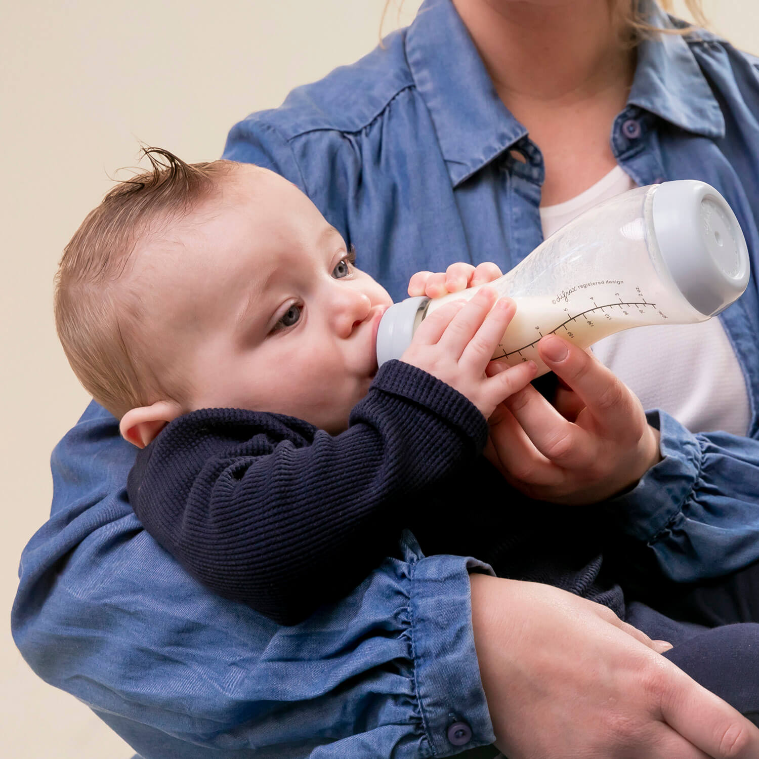 Baby drinkt uit Difrax glazen S-fles kleur Ice (blauw) in de armen van moeder – anti-colic glazen babyfles voor baby's