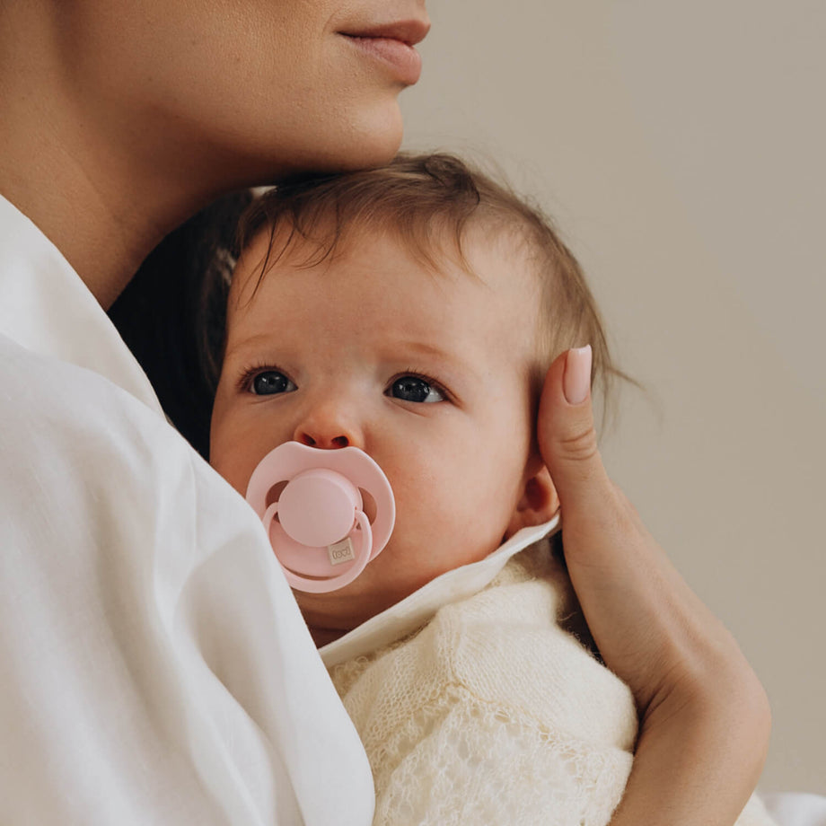 Moeder houdt een baby vast met een roze LOVI Dynamic fopspeen (Tutti Frutti, Rose)
