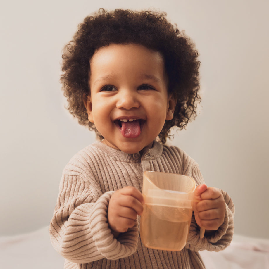 Lachende peuter houdt een Difrax LOVI oefenbeker vast met beide handjes – ideaal voor zelfstandig leren drinken.