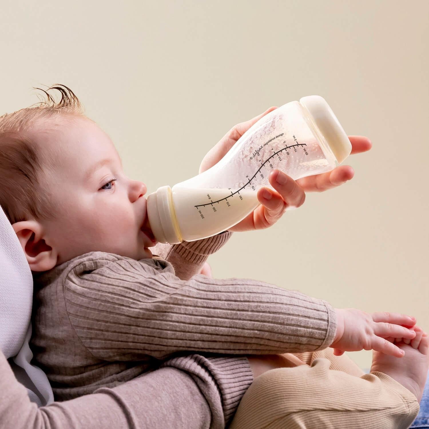 Baby drinkt uit Difrax S-fles glas 250ml Popcorn terwijl ouder de fles vasthoudt - de ergonomische S-vorm zorgt voor een natuurlijke drinkhouding