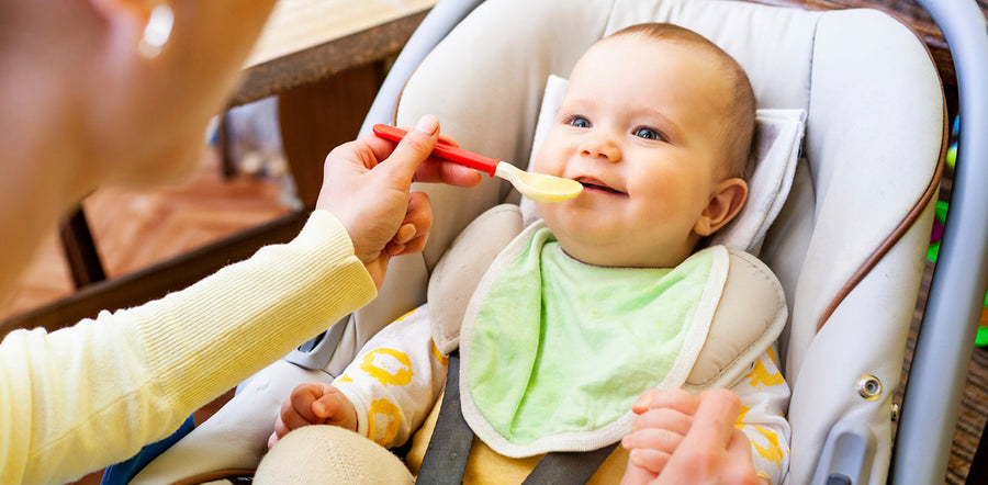 Une mère nourrit son petit enfant avec une cuillère pour bébé, en lui donnant à manger avec douceur pendant que l’enfant est assis et ouvre la bouche pour manger.