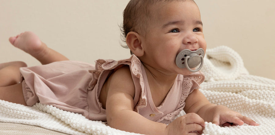 Bébé allongé sur le ventre avec une sucette en bouche, calme et détendu.