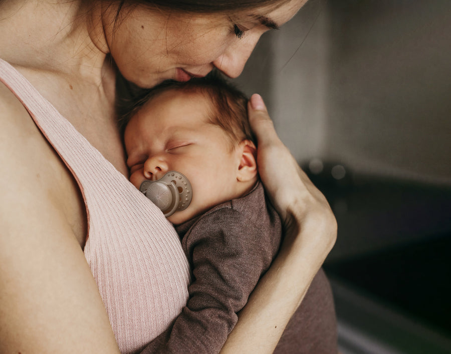 Moeder houdt haar slapende baby met fopspeen liefdevol tegen zich aan.