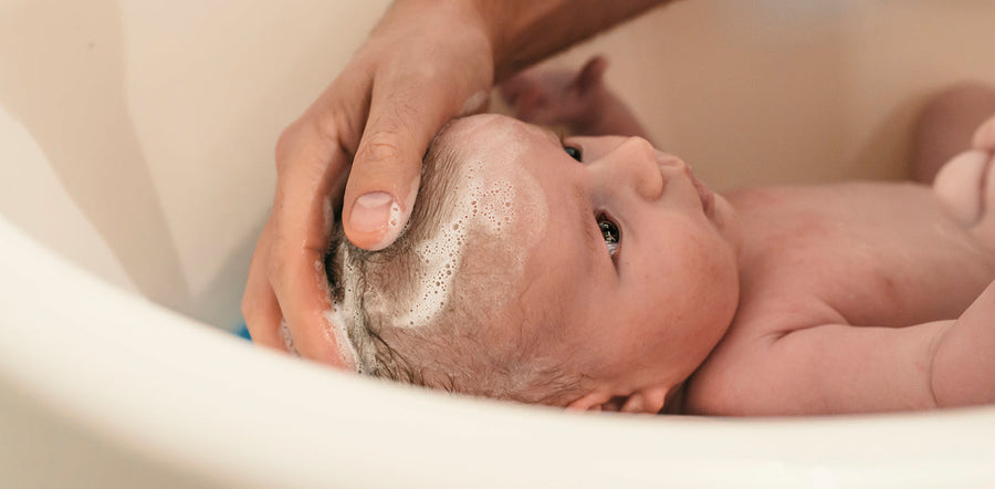 Bébé prenant son bain, soutenu avec douceur par un parent — un moment de soin et de tendresse illustrant l’importance de la préparation et du calme lors du bain du nouveau-né.