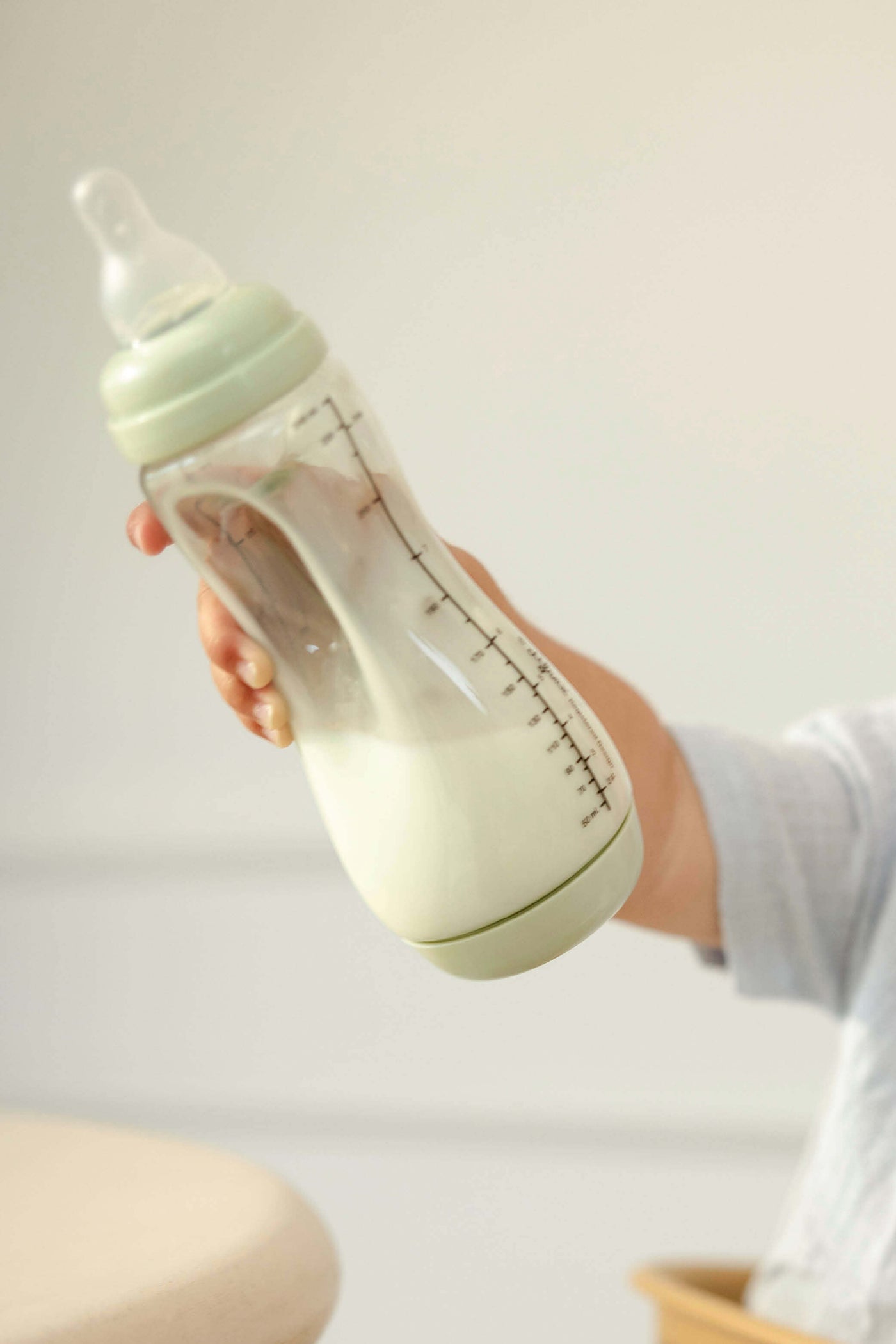 Baby houdt enthousiast Difrax Easy Grip pistachgroene fles omhoog, zelfstandig drinken met natuurlijke speen