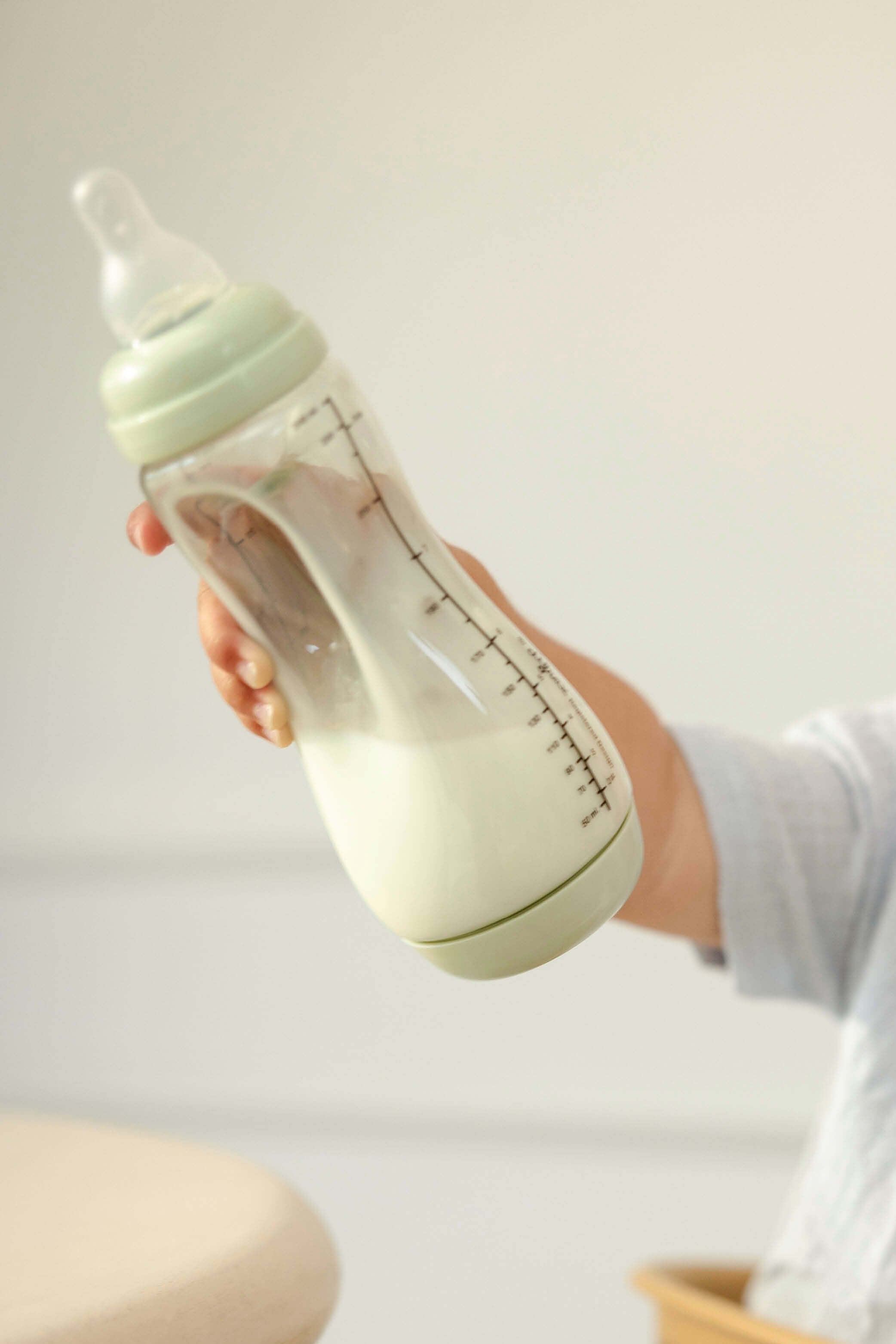 Baby houdt enthousiast Difrax Easy Grip pistachgroene fles omhoog, zelfstandig drinken met natuurlijke speen