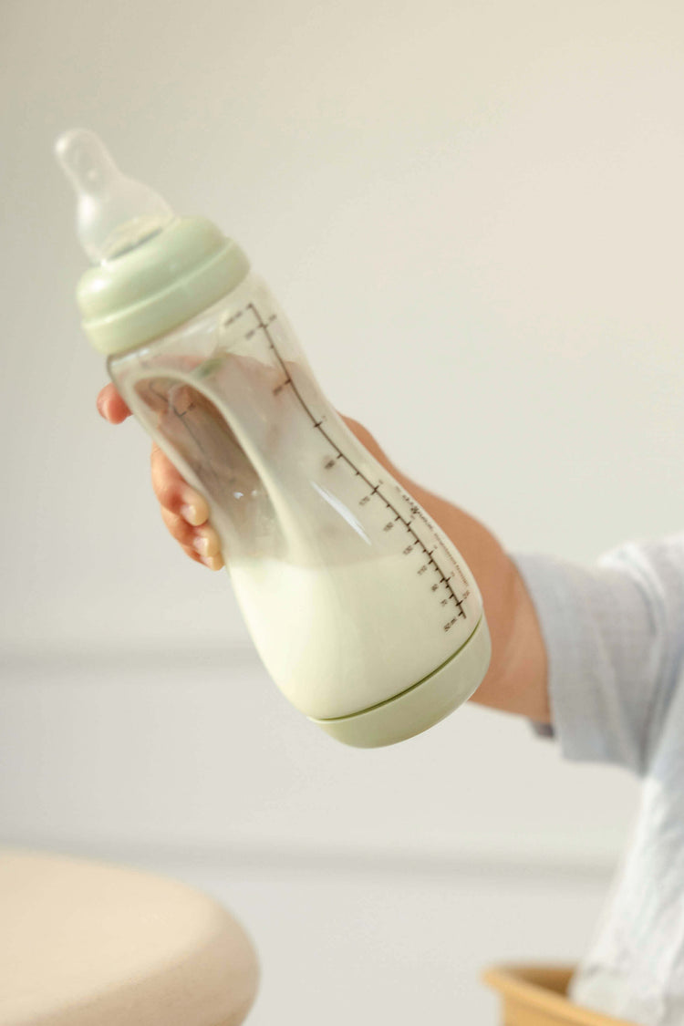 Baby houdt enthousiast Difrax Easy Grip pistachgroene fles omhoog, zelfstandig drinken met natuurlijke speen