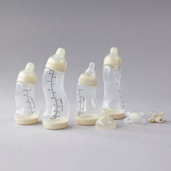 Difrax Newborn Starter Set compleet uitgepakt: 4 S-flesjes in ivory en 2 transparante fopspenen op grijze achtergrond