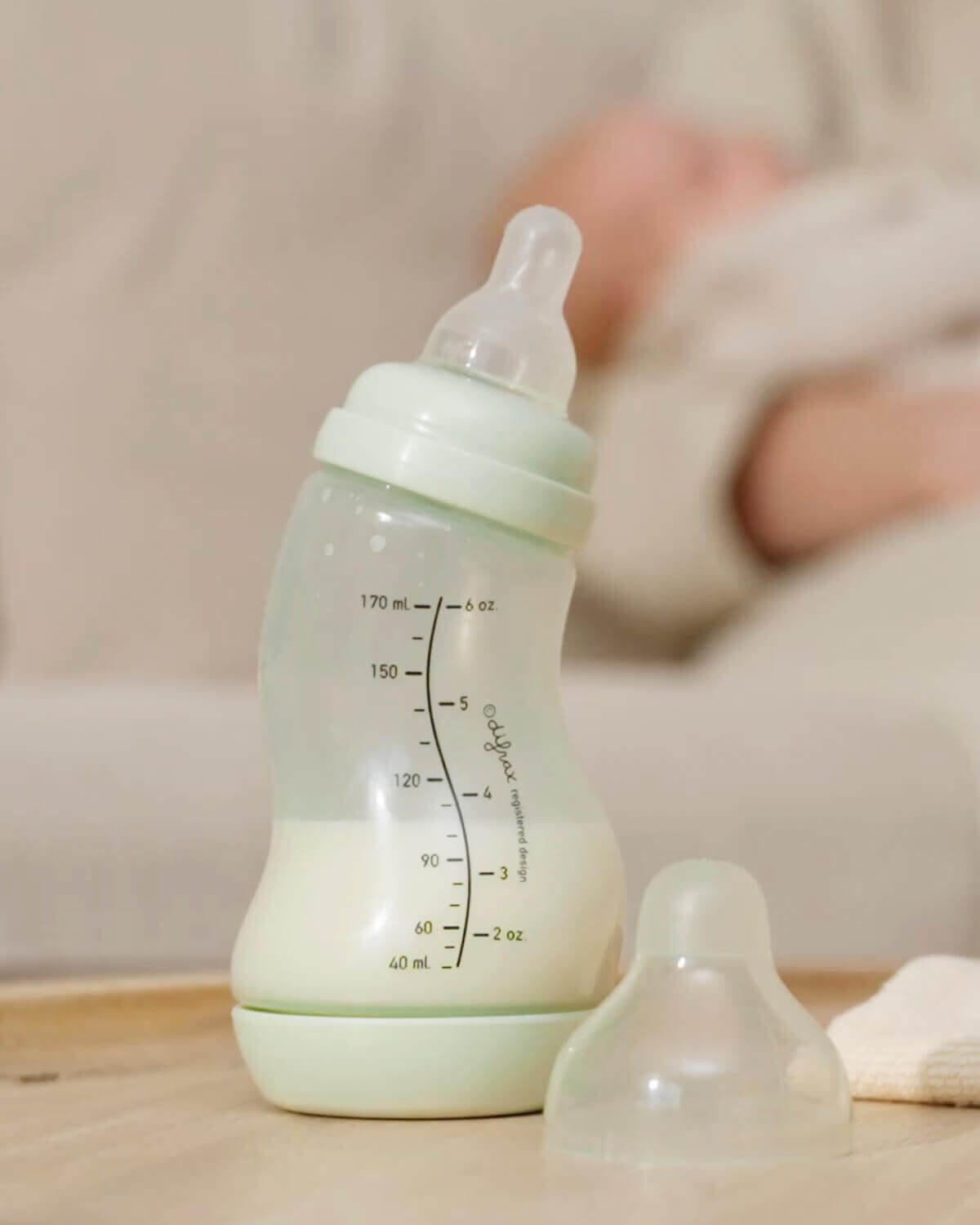 Pistachgroene Difrax S-fles met extra speen op voorgrond, slapende baby op de achtergrond, kalme voedingsomgeving