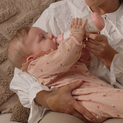 Baby in roze kleding wordt gevoed met Pink Opal Difrax S-fles 250ml, liefdevolle voedingssituatie op zachte ondergrond