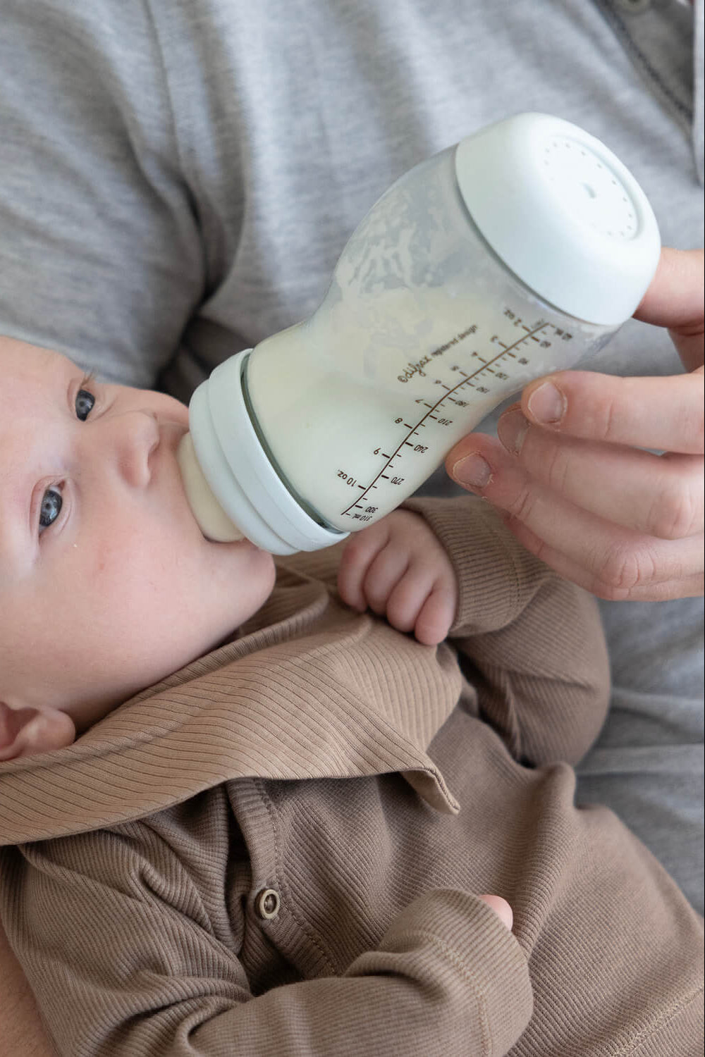 Pasgeboren baby wordt gevoed met ijsblauwe Difrax S-fles 310ml, intieme close-up van natuurlijk voedingsmoment