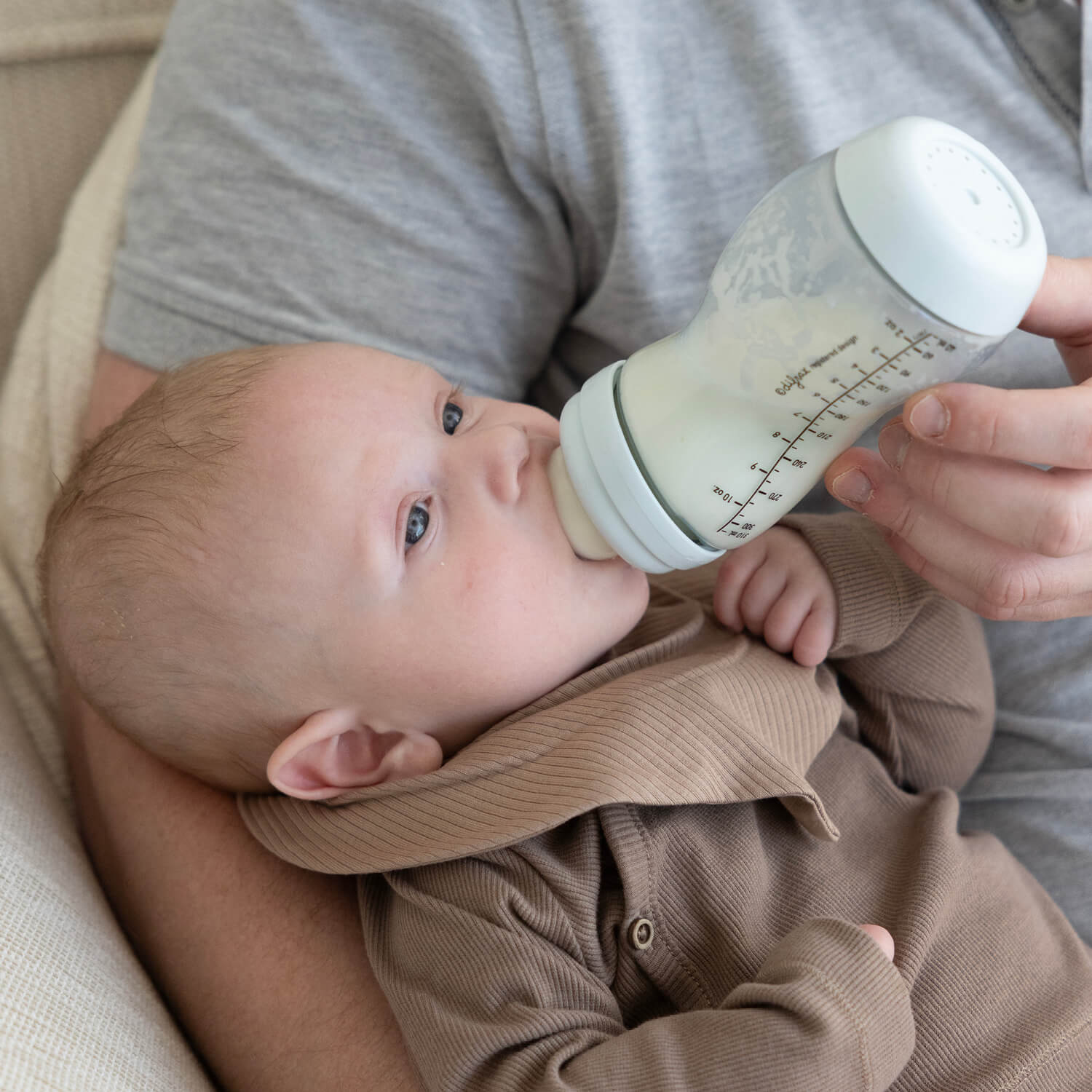 Pasgeboren baby wordt gevoed met ijsblauwe Difrax S-fles 310ml, intieme close-up van natuurlijk voedingsmoment