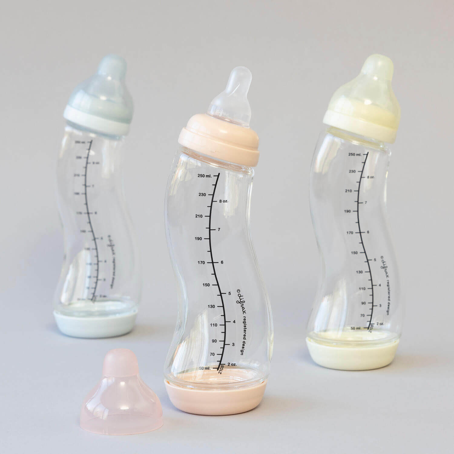 Drie Difrax glazen S-flesjes 250ml in de kleuren blauw, roze en naturel met losse Natural speen op grijze achtergrond