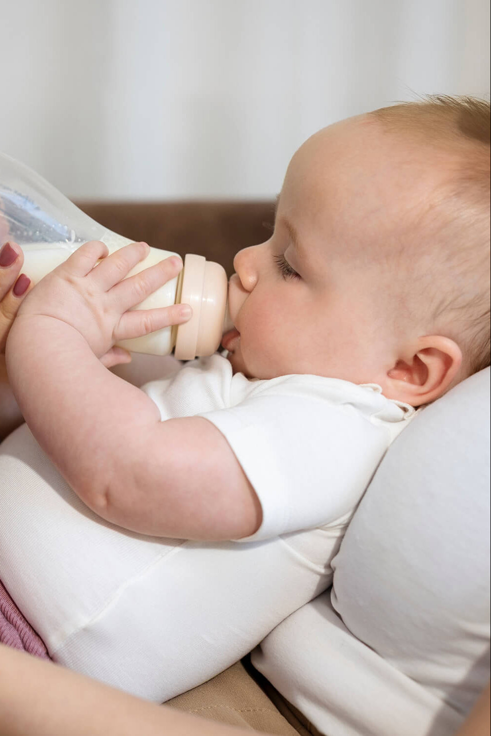 Baby drinkt uit Difrax glazen S-fles kleur Blossom (roze) terwijl moeder de fles vasthoudt – anti-colic glazen babyfles
