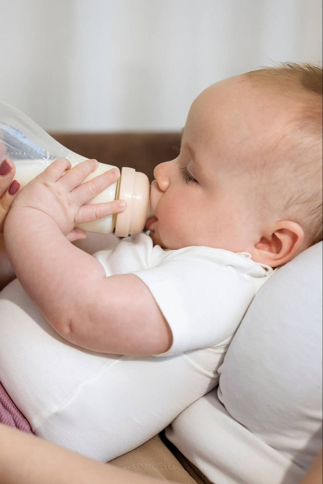Baby drinkt uit Difrax glazen S-fles kleur Blossom (roze) terwijl moeder de fles vasthoudt – anti-colic glazen babyfles