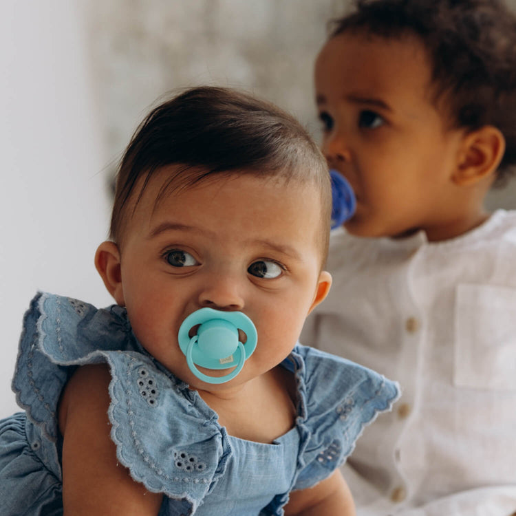 Twee baby's naast elkaar; de voorste met een aqua Difrax LOVI Dynamic fopspeen (Tutti Frutti, Aqua Green)