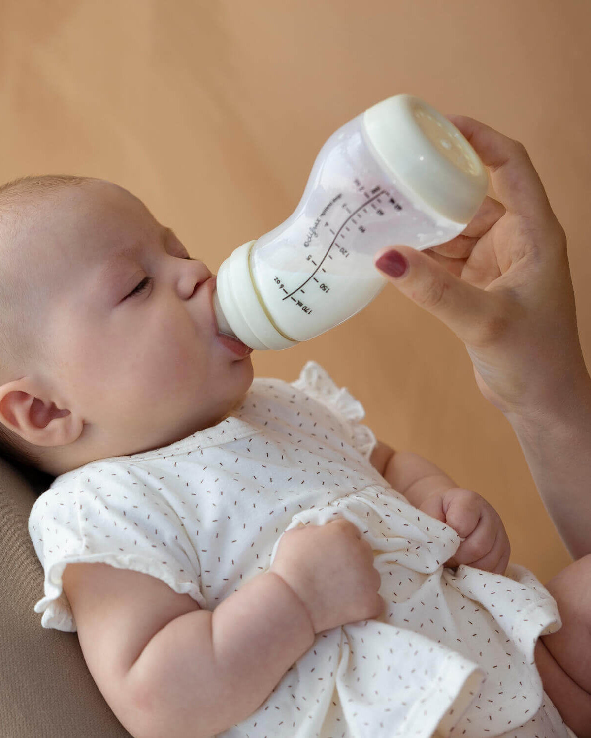 Baby wordt gevoed met ivoorkleurige Difrax S-fles, rustgevende setting met pasgeboren in wit kleding