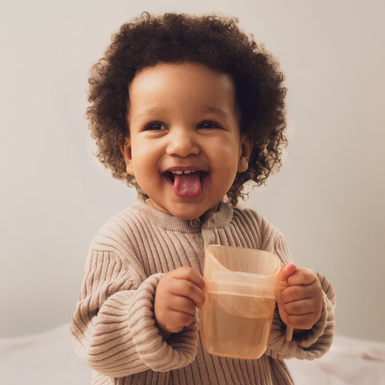 Lachende peuter houdt een Difrax LOVI oefenbeker vast met beide handjes – ideaal voor zelfstandig leren drinken.