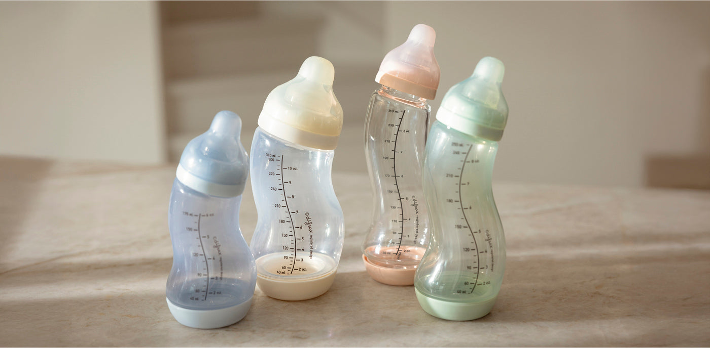 Vier glazen Difrax S-flessen in pastelkleuren blauw, ivoor, roze en mintgroen op houten ondergrond